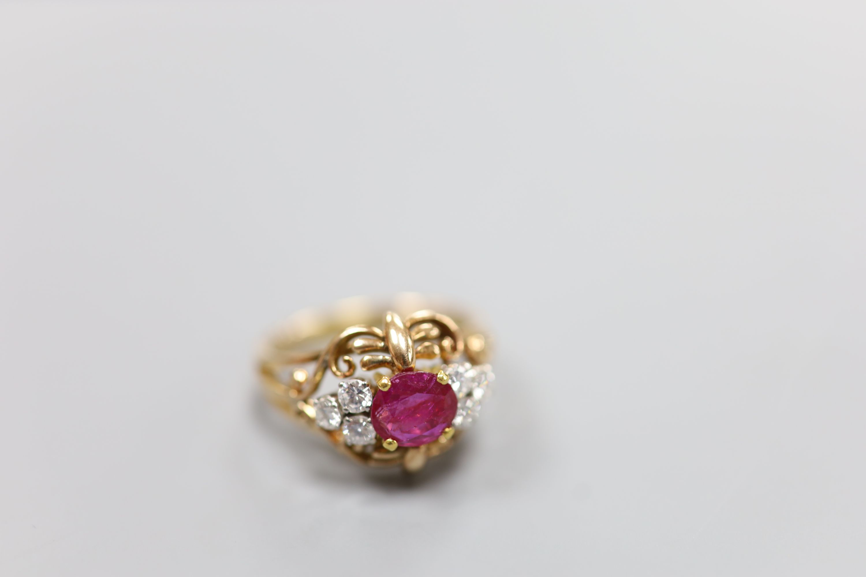 A stylish yellow metal, ruby and diamond set cluster ring, with single round cut ruby(crack), flanked by six round cut diamonds, in an openwork scroll setting, size Q/R, gross weight 7.5 grams, in a Cartier box.